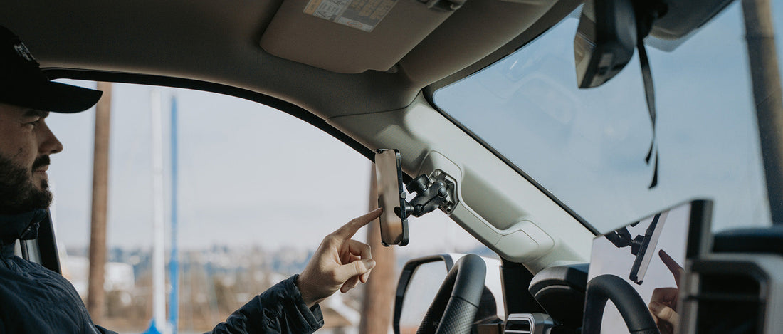 A man using his iPhone 14 that is secured to his car's grab handle with the new RAM form-fit holder. 
