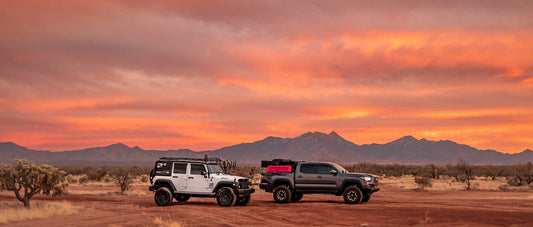 A white jeep wrangler and grey toyota tacoma in the desert during a stunning orange and pink sunset