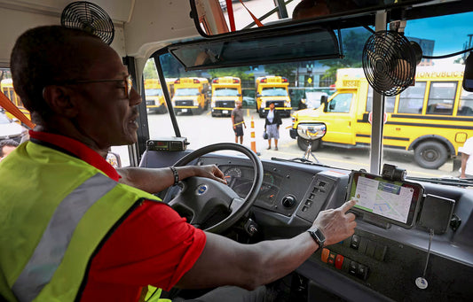 A male bus driver is sitting in the drivers seat interacting with a Samsung Tab Active3 in a RAM Mounts docking station