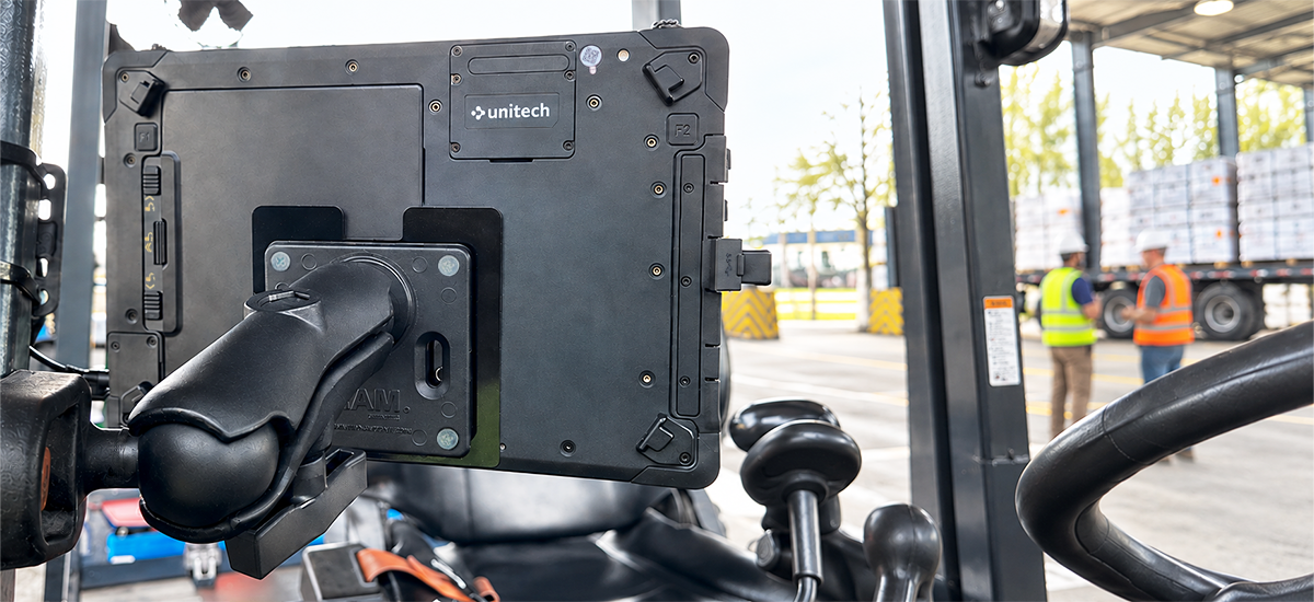 Rear view of a Unitech WM11 10-inch rugged tablet secured inside a forklift using a RAM® 75x75mm VESA Plate, C Size Medium Double Socket Arm, and Square Post Clamp Base, providing an adjustable tablet mounting solution for warehouse operations.