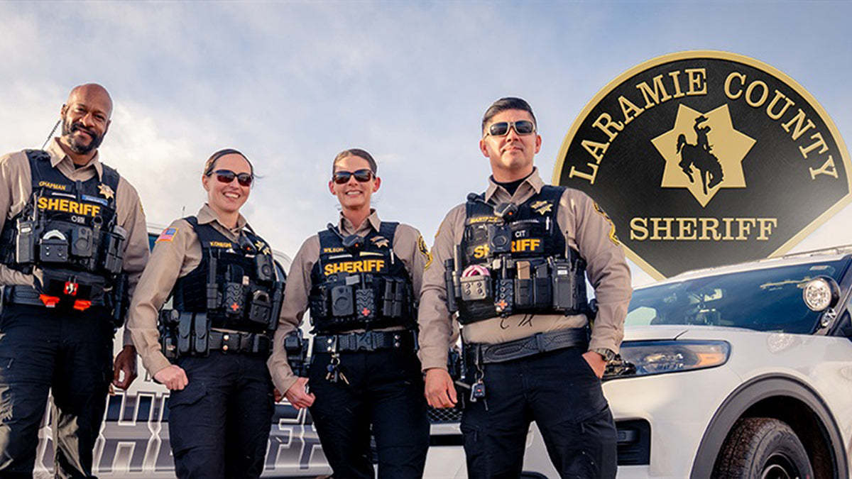 Four police officers, 2 men and 2 women, are standing in front of a police cruiser looking towards the camera.