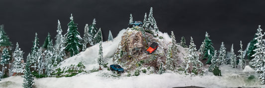 A snowy, forest miniatures scene with a large mountain in the middle with three cars off-roading. Includes a Ford Bronco, Rivian Truck, and Jeep
