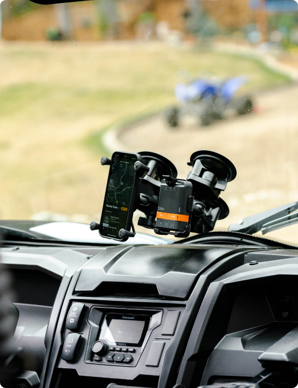 Smartphone displaying topographic map secured in RAM® X-Grip® holder with dual suction cup mounts attached to vehicle windshield, positioned above dashboard entertainment system for hands-free GPS navigation during off-road driving.