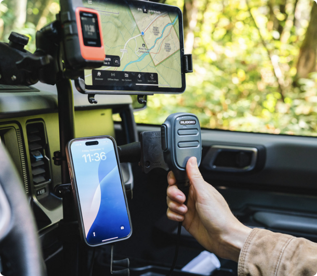 Tablet displaying detailed navigation map with GPS route secured in RAM® mount system attached to vehicle dashboard, alongside smartphone showing 11:36 time in the magnetic RAM® holder and driver's hand operating radio microphone, demonstrating comprehensive mobile communication and navigation setup for off-road applications.