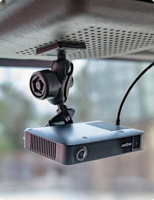 Motive AIDC+ fleet camera suspended from a vehicle headliner using a RAM® overhead mounting solution. The adjustable ball-and-socket mount positions the camera for an unobstructed forward-facing view while integrated cable routing keeps the installation organized. The image highlights a secure, low-profile mounting solution for commercial fleet video telematics and driver monitoring systems.