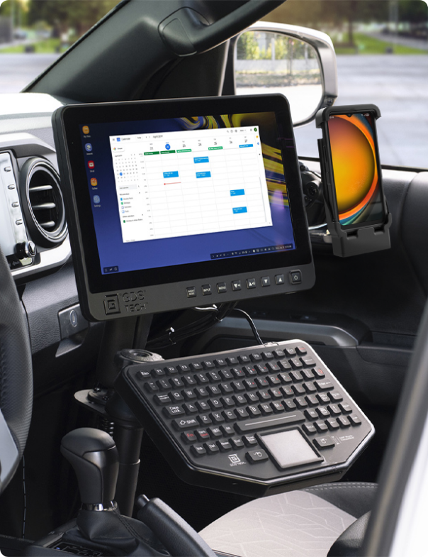 Interior of a vehicle featuring a mounted GDS Tech monitor displaying a digital calendar, a rugged keyboard with a trackpad, and a smartphone in a RAM mount.