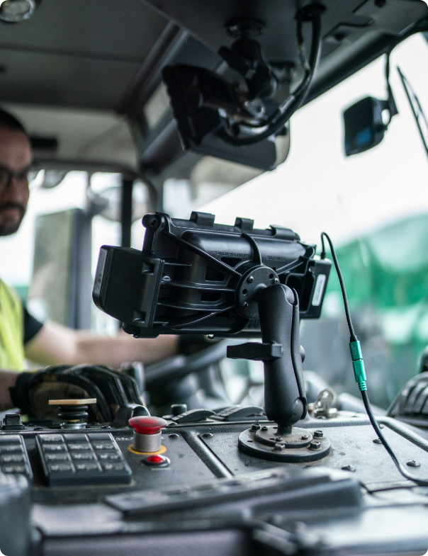 RAM® GDS vehicle dock cradle with IntelliSkin technology mounted on heavy equipment operator console with power cable connection, positioned among control buttons and joystick for secure tablet mounting during waste management operations with operator visible in background.