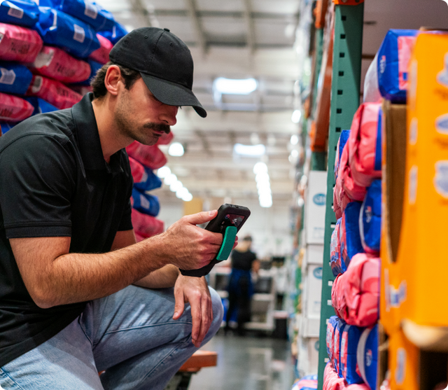 Image of a worker man kneeling down in a grocery store with an IntelliSkin-wrapped Zebra EM45 RFID