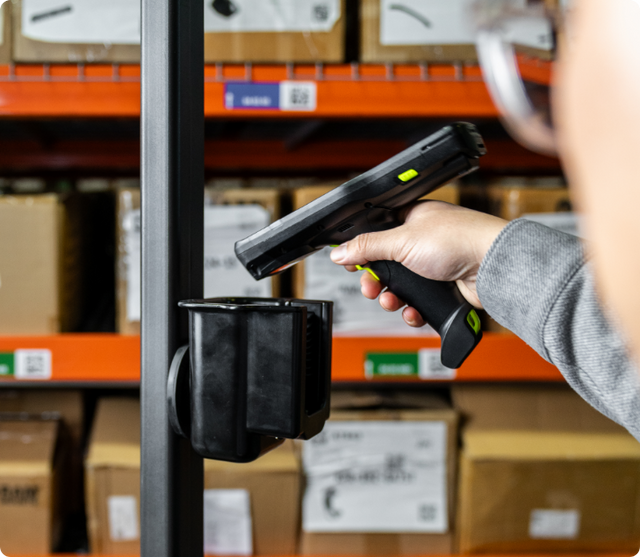 Image of a person inserting the MC3400 Scanner gun into the RAM Power-Grip universal scanner gun holder with a magnetic mount installed on a forklift in a warehouse